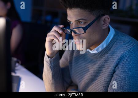 Asian businessman holding eyeglasses while looking at computer screen while working in office. Technology, focus, unaltered, business, corporate, work Stock Photo