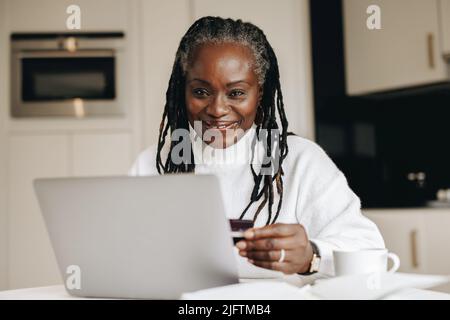 Happy mature woman smiling at the camera while making an online payment with a credit card. Ethnic senior woman doing some online shopping for her fre Stock Photo