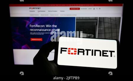 Person holding smartphone with logo of US cybersecurity company Fortinet Inc. on screen in front of website. Focus on phone display. Stock Photo