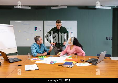 Manager looking at multiracial colleagues discussing strategy in meeting at creative office Stock Photo