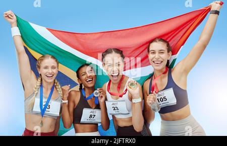 Portrait diverse group of female olympic athletes holding winners medals and African flag. Happy and proud champions of South Africa. Winning a medal Stock Photo