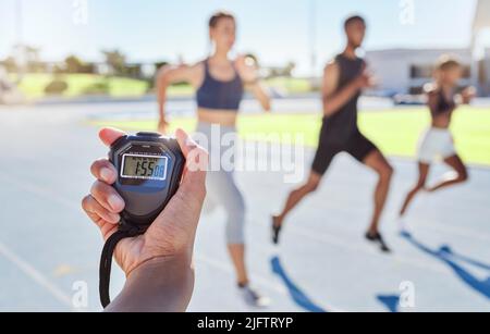 A sport coach timing athletes progress using a stopwatch. .Blurred athletes racing towards finish line and breaking the record. Stopwatch measuring Stock Photo