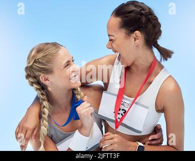Two cheerful athletic women embracing while holding gold medals from competing in sports event. Joyful fit active athletes feeling proud after winning Stock Photo