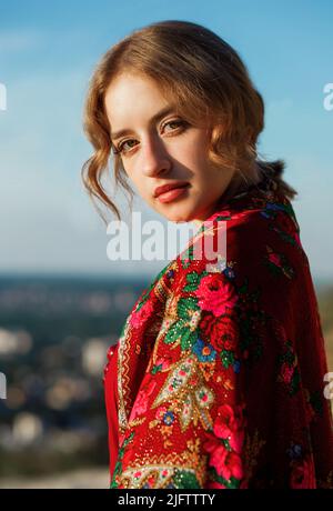 Beautiful girl in traditional ethnic dress with a red floral kerchief on her back posing on the mountain. Stock Photo