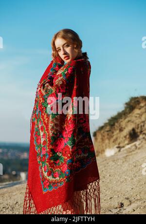 Beautiful girl in traditional ethnic dress with a red floral kerchief on her back posing on the mountain. Stock Photo