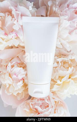 Mock-up of white squeeze bottle plastic tube and pastel pink peony. Top view, Flat lay style. Natural organic cosmetics concept Stock Photo