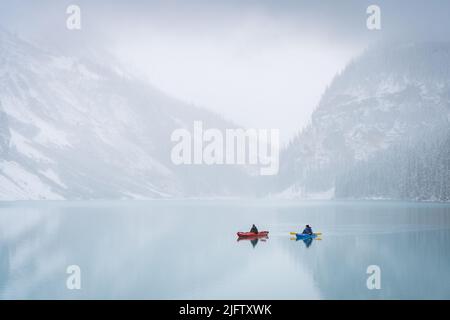 Two kayakers on azure alpine lake shrouded by mist during early winter, Banff N. Park, Canada Stock Photo
