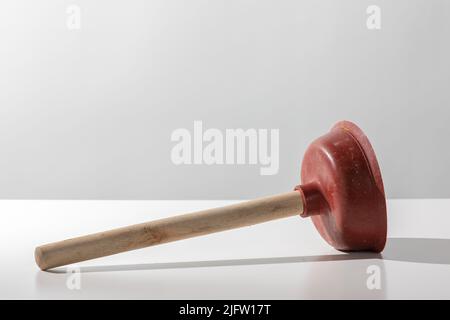 Old used red toilet plunger with wooden handle on a white background Stock Photo