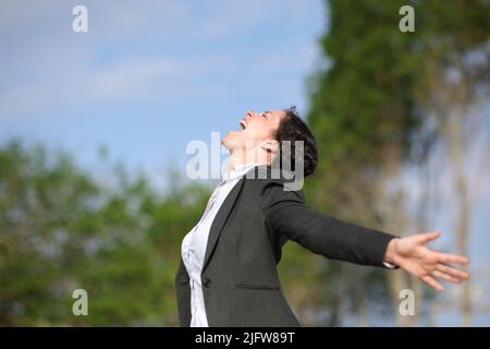 Side view portrait of an excited businesswoman outstrstching arms in a park Stock Photo