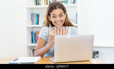 Laughing mature adult female teacher schooling online at computer at home or at office Stock Photo