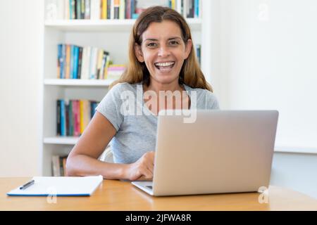 Laughing mature adult female teacher working at computer at home or at office Stock Photo