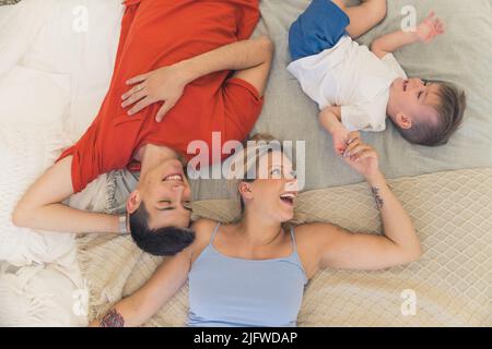 Young family having fun, laughing, ticking each other. Curious little boy tries to escape the ticking. Engaged father and mother. High quality photo Stock Photo