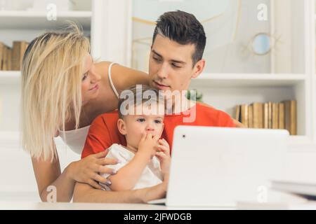 young couple watching something in the laptop with their little son, medium closeup indoor family concept. High quality photo Stock Photo