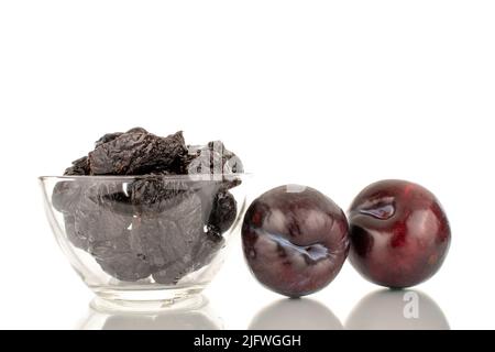 Two ripe fresh black plums and a few prunes in a glass bowl, close-up, isolated on a white background. Stock Photo