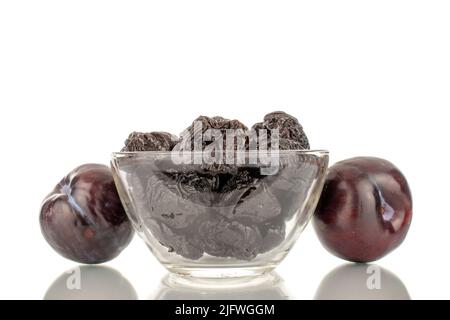 Two ripe fresh black plums and a few prunes in a glass bowl, close-up, isolated on a white background. Stock Photo