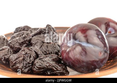 Two fresh black plums and a few prunes on a clay dish, close-up, isolated on a white background. Stock Photo