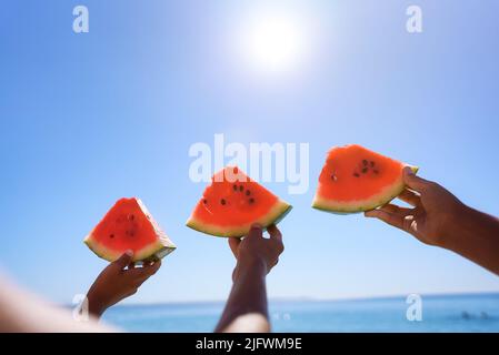 Three hands with watermelon segments are on azure calm sea water background. Stock Photo
