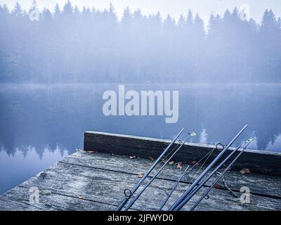 A closeup of fishing rods on a wooden surface near the pier of the lake Stock Photo