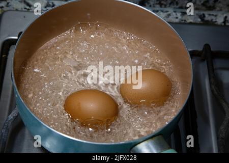 Chicken eggs boiling in water in a light blue saucepan on the stove. Stock Photo