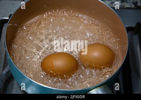 Chicken eggs boiling in water in a light blue saucepan on the stove. Stock Photo