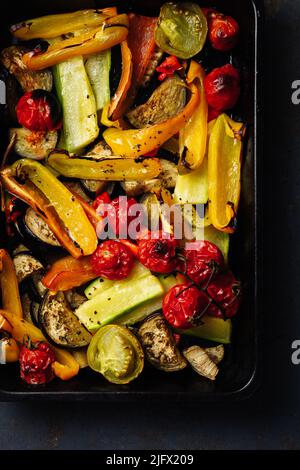 Roasted sliced vegetables on a baking tray. Oven-baked tomatoes, eggplants, zucchini, bell peppers. Stock Photo