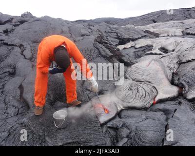 An  Hawaiian Volcano Observatory geologist shields his face from intense heat as he dips a rock hammer into an active p?hoehoe toe. After scooping out the lava it is placed in the water to quench it. HVO routinely collects lava samples for chemical analysis, which can give insight into changes in the magmatic system. Credit: USGS Stock Photo