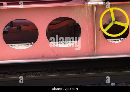 Partial view of the side of a solid steel railroad low loader wagon with visible yellow turning wheel and mechanism for locking the brakes when parked Stock Photo