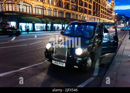 Taxi in front of Harrods department store. Harrods Limited is a department store located on Brompton Road in Knightsbridge. It is owned by the state o Stock Photo