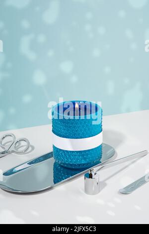 A bright blue soy wax candle in a glass on the silver plate. A candle in blue glass, a silver plate and snuffer on a white table. Cozy atmosphere Stock Photo