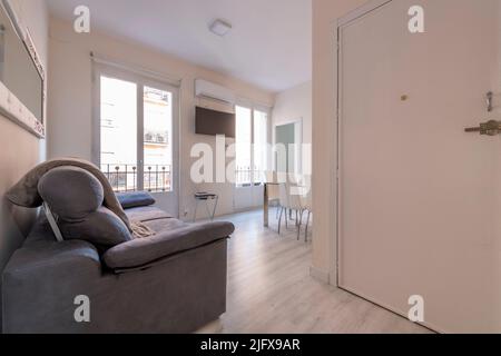 Entrance hall and corridor of a house with light wood parquet flooring, large balconies with wooden doors and metal railings and a sofa in the foregro Stock Photo