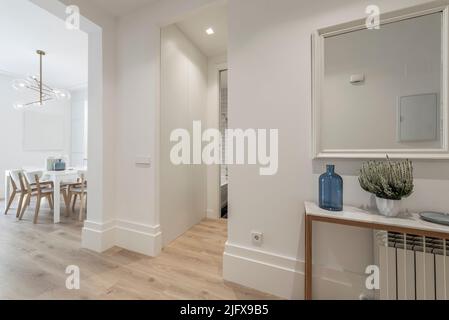 Entrance hall and housing distributor with light wood flooring, white wood carpentry, metal and marble sideboard and mirror and entrance to several ro Stock Photo