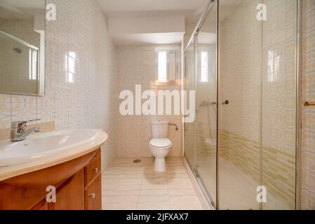 Bathroom decorated with square walk-in shower with cherry wood cabinets with frameless mirror and white porcelain sink Stock Photo