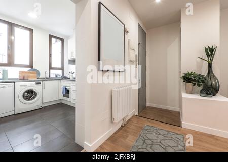 Entrance hall of a house with an open kitchen with white furniture with gray stoneware floors and a living room with wooden floors Stock Photo