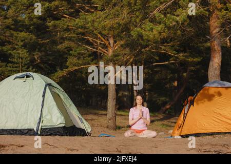 A woman meditates in front of a pine forest. Stock Photo