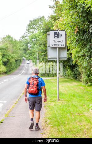 Man walking along a road  pavement  under a road sign saying speed cameras Stock Photo