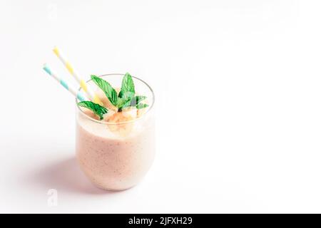 Banana smoothie with straw and mint leaf on white background. Healthy vegan food. Stock Photo
