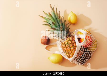 Pineapple, lemons, oranges and kiwi fruits in a string bag. Zero waste concept, healthy food. Top view, flat lay. Stock Photo