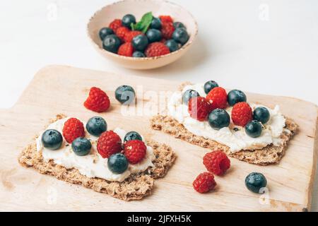 Sandwiches with blueberries and raspberries on cutting board on white wooden table. Healthy breakfast. Top view. Stock Photo