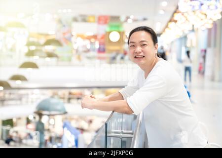 Orange Light effect in image of Asian long hair man who stands and smile in front of terrace in deparment store. it sparkles nicely picture. Stock Photo