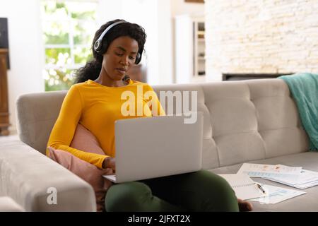 African american young female freelancer using headphone while working on laptop at home, copy space Stock Photo