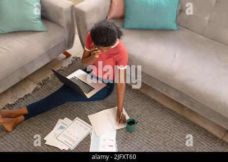 Young african american female freelancer discussing project while talking on smart phone by sofa Stock Photo