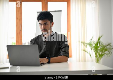 Smart and handsome asian male office worker or tech engineer using laptop computer in the modern office. Stock Photo