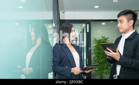 Business people holding digital tablet and talking to each other. Office workplace setting. Stock Photo