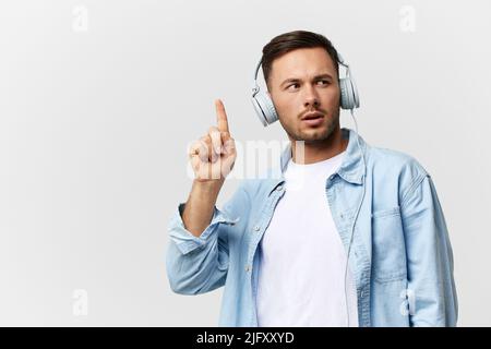 Thoughtful pensive excited tanned handsome man in casual basic t-shirt headphones hold fingers up posing isolated on over white studio background Stock Photo