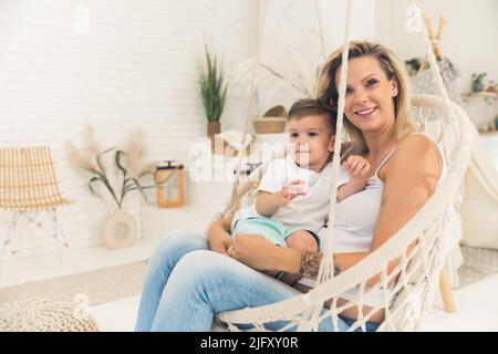 little Caucasian boy and his pregnant mother sitting in the hammock at home, medium full shot. High quality photo
