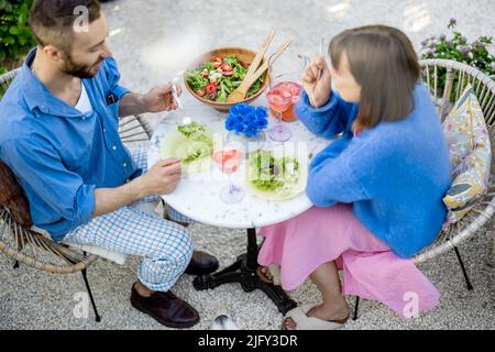 Young man and woman have a lunch with healthy salad and drink outdoors Stock Photo