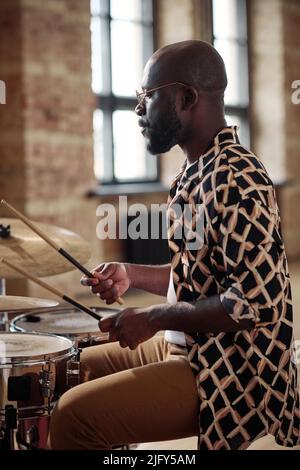 African young musician sitting at drums set at studio and playing drums with stick Stock Photo