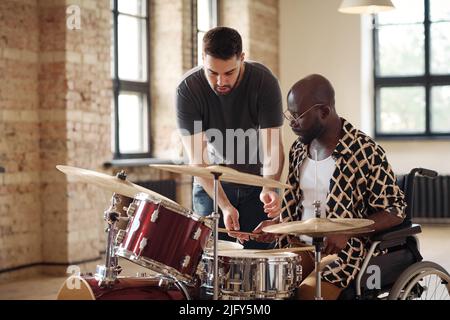 African young man with disability learning to play drums with drummer teaching him at studio Stock Photo