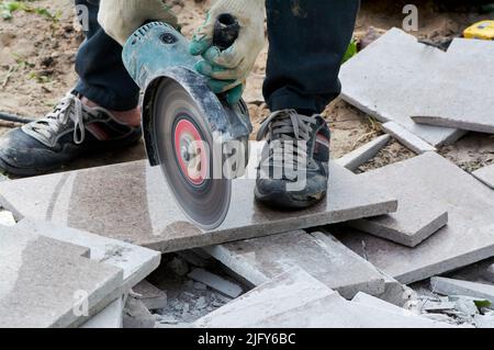 A worker with a circular saw cuts a tile in close-up. Stock Photo