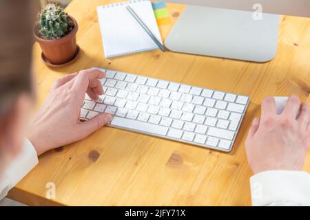 workspace of an office employee and female hands on the keyboard. monitor, mouse, notebook, plant Stock Photo
